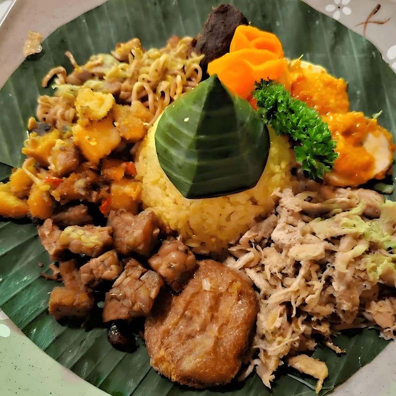 A vibrant Japanese dish with yellow rice, various meats, vegetables, and a banana leaf garnish.