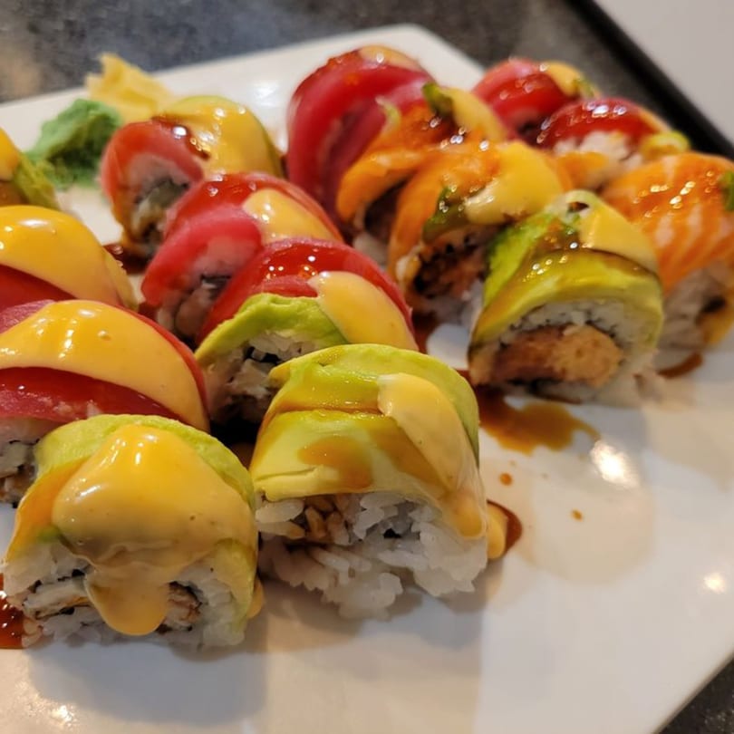A close-up of colorful sushi rolls with various toppings and sauces on a white plate.