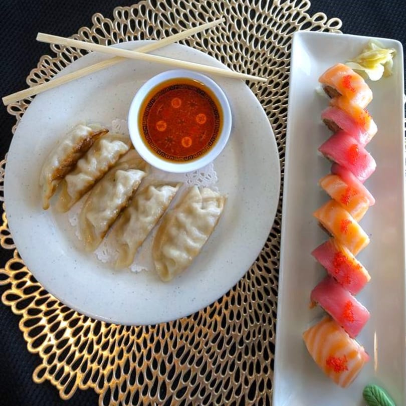 Osaka Hibachi's gyoza with dipping sauce and a colorful sushi roll on a gold placemat.
